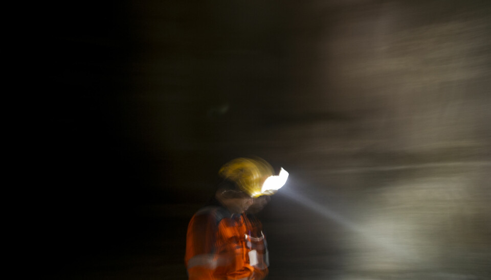 En arbetare med gul hjälm och pannlampa i en mörk gruva